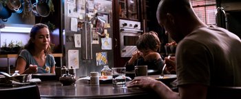 Movie still from “I Am Legend” (2007), directed by Francis Lawrence – A group of people sitting at a table in a kitchen; Medium shot, Over the shoulder angle