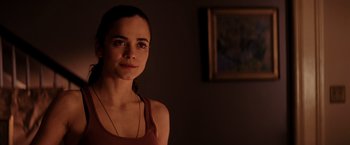 Movie still from “I Am Legend” (2007), directed by Francis Lawrence – A woman in a brown tank top standing next to a painting; Close Up shot, Over the shoulder angle