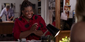 Movie still from “I Believe in Santa” (2022), directed by Alex Ranarivelo – A woman sitting at a dining table clapping her hands; Medium shot, Over the shoulder angle