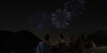Movie still from “I Believe in Santa” (2022), directed by Alex Ranarivelo – A group of people watching fireworks at night; Extreme Wide shot, Overhead angle