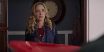 Movie still from “I Believe in Santa” (2022), directed by Alex Ranarivelo – A woman sitting at a table in front of a red clock; Close Up shot, Over the shoulder angle