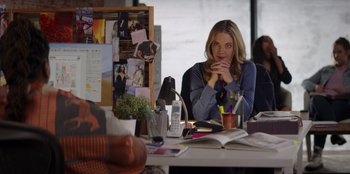 Movie still from “I Believe in Santa” (2022), directed by Alex Ranarivelo – A woman sitting at a table with a book; Medium shot, Over the shoulder angle