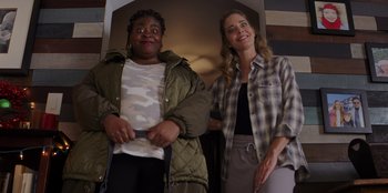 Movie still from “I Believe in Santa” (2022), directed by Alex Ranarivelo – Two women standing next to each other in a room; Medium shot, Low angle