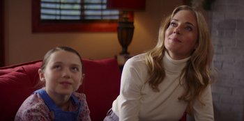 Movie still from “I Believe in Santa” (2022), directed by Alex Ranarivelo – A woman sitting next to a young girl on a red couch; Close Up shot, Over the shoulder angle
