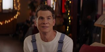 Movie still from “I Believe in Santa” (2022), directed by Alex Ranarivelo – A person wearing suspenders with lights in the background; Close Up shot, Over the shoulder angle
