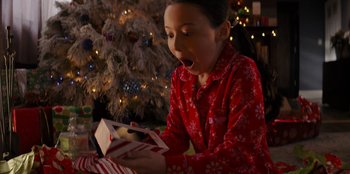 Movie still from “I Believe in Santa” (2022), directed by Alex Ranarivelo – A little girl opening a christmas present in front of a christmas tree; Close Up shot, High angle