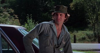 Movie still from “I Spit on Your Grave” (1978), directed by Meir Zarchi – A man wearing a hat standing in front of a car; Medium shot, Low angle