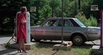 Movie still from “I Spit on Your Grave” (1978), directed by Meir Zarchi – A woman in a red dress standing in front of a car; Wide shot, Over the shoulder angle