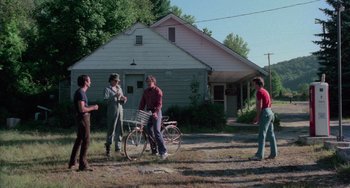 Movie still from “I Spit on Your Grave” (1978), directed by Meir Zarchi – A group of people standing in a yard with a bicycle; Wide shot, Over the shoulder angle