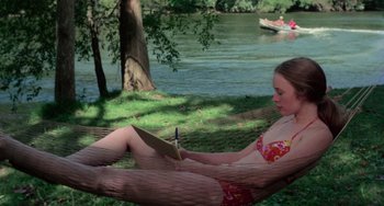 Movie still from “I Spit on Your Grave” (1978), directed by Meir Zarchi – A girl in a bikini is sitting in a hammock reading a book; Wide shot, High angle