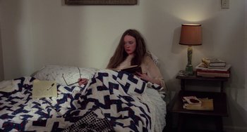 Movie still from “I Spit on Your Grave” (1978), directed by Meir Zarchi – A woman sitting on a bed reading a book; Medium shot, High angle