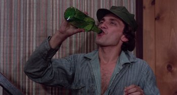 Movie still from “I Spit on Your Grave” (1978), directed by Meir Zarchi – A man in a hat is drinking from a green bottle; Close Up shot, Low angle