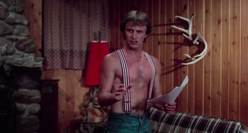 Movie still from “I Spit on Your Grave” (1978), directed by Meir Zarchi – A shirtless man holding a piece of paper in his hand; Medium shot, Over the shoulder angle