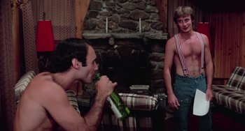 Movie still from “I Spit on Your Grave” (1978), directed by Meir Zarchi – A man drinking a beer while another man stands by the fire place; Medium shot, Over the shoulder angle