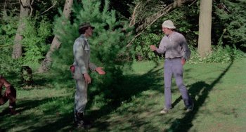 Movie still from “I Spit on Your Grave” (1978), directed by Meir Zarchi – Two men are talking in the grass near a tree; Wide shot, Over the shoulder angle