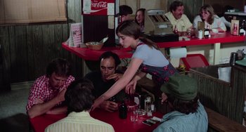 Movie still from “I Spit on Your Grave” (1978), directed by Meir Zarchi – A woman standing at a table in front of a group of diners; Medium shot, High angle