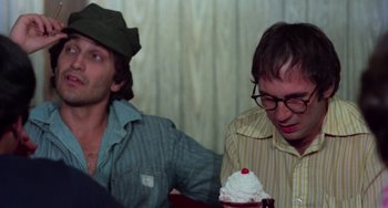 Movie still from “I Spit on Your Grave” (1978), directed by Meir Zarchi – Two young men sitting at a table with a cupcake; Close Up shot, Over the shoulder angle