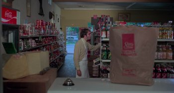 Movie still from “I Spit on Your Grave” (1978), directed by Meir Zarchi – A man in a store looking at a shelf of drinks; Wide shot, Low angle