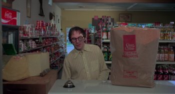 Movie still from “I Spit on Your Grave” (1978), directed by Meir Zarchi – A man sitting at a table in a grocery store; Medium shot, Low angle