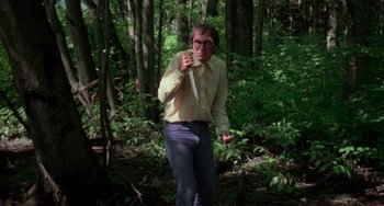 Movie still from “I Spit on Your Grave” (1978), directed by Meir Zarchi – A man standing in the middle of a forest holding a stick; Medium shot, Low angle