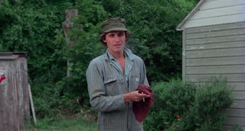 Movie still from “I Spit on Your Grave” (1978), directed by Meir Zarchi – A man in a hat holding a towel in his hands; Medium shot, Low angle