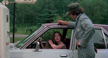 Movie still from “I Spit on Your Grave” (1978), directed by Meir Zarchi – A woman sitting in the drivers seat of a car while a man stands next to it; Medium shot, Over the shoulder angle
