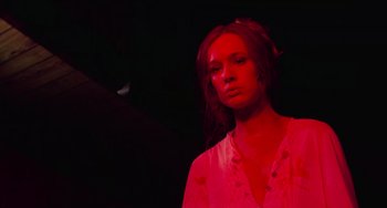 Movie still from “I Spit on Your Grave” (1978), directed by Meir Zarchi – A woman in a white shirt is standing in a dark room; Medium shot, Low angle
