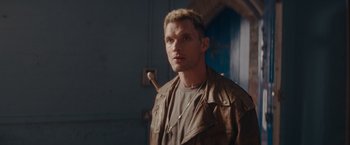 A man in a brown jacket is standing in a room