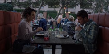 Movie still from “I Want You Back” (2022), directed by Jason Orley – A group of people sitting at a wooden table; Medium shot, Over the shoulder angle