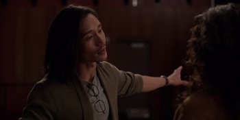 Movie still from “I Want You Back” (2022), directed by Jason Orley – A man with long black hair wearing glasses and a brown jacket; Medium shot, Over the shoulder angle