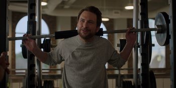 Movie still from “I Want You Back” (2022), directed by Jason Orley – A man is holding onto a bar in a gym; Medium shot, Over the shoulder angle
