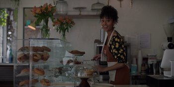 Movie still from “I Want You Back” (2022), directed by Jason Orley – A woman standing in front of a display case in a pastry shop; Medium shot, Over the shoulder angle