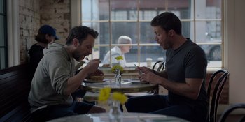 Movie still from “I Want You Back” (2022), directed by Jason Orley – A couple of men sitting at a table with food; Medium shot, Over the shoulder angle