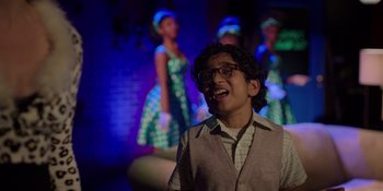 Movie still from “I Want You Back” (2022), directed by Jason Orley – A young man wearing glasses standing in front of a group of people; Medium shot, High angle
