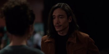 Movie still from “I Want You Back” (2022), directed by Jason Orley – A man with long black hair wearing a brown jacket; Close Up shot, Over the shoulder angle