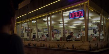 Movie still from “I Want You Back” (2022), directed by Jason Orley – People are sitting at a restaurant at night time; Extreme Wide shot, Low angle