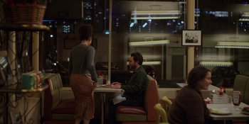 Movie still from “I Want You Back” (2022), directed by Jason Orley – A man and a woman sitting at a table in front of a window; Wide shot, Over the shoulder angle