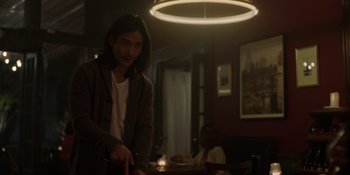 Movie still from “I Want You Back” (2022), directed by Jason Orley – A man standing in front of a table in a room; Medium shot, Over the shoulder angle
