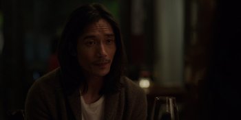 Movie still from “I Want You Back” (2022), directed by Jason Orley – A man with long hair sitting at a table with a glass of wine; Close Up shot, Over the shoulder angle