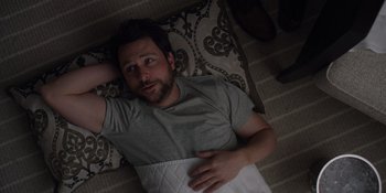 Movie still from “I Want You Back” (2022), directed by Jason Orley – A man laying in a bed with a pillow on top of him; Medium shot, Overhead angle