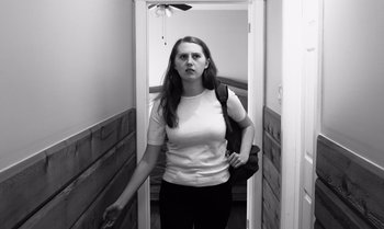Movie still from “I'm Sorry If I Took a Toll on You” (2021), directed by Jake Burgess – A woman standing in a hallway with a backpack; Medium shot, Low angle