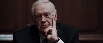Movie still from “Imagine That” (2009), directed by Karey Kirkpatrick – An older man wearing a suit and tie with his hand under his chin; Close Up shot, Over the shoulder angle