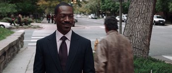 Movie still from “Imagine That” (2009), directed by Karey Kirkpatrick – A man wearing a suit and tie standing on a sidewalk; Close Up shot, Over the shoulder angle