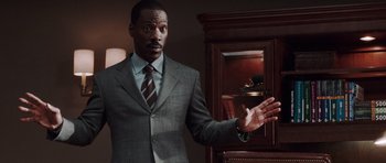 Movie still from “Imagine That” (2009), directed by Karey Kirkpatrick – A man in a suit and tie standing in front of a cabinet; Medium shot, Over the shoulder angle