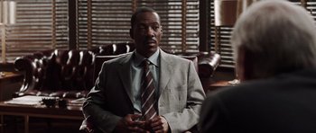 Movie still from “Imagine That” (2009), directed by Karey Kirkpatrick – A man wearing a suit and tie sitting in front of a window; Medium shot, Over the shoulder angle