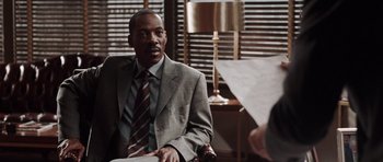 Movie still from “Imagine That” (2009), directed by Karey Kirkpatrick – A man in a suit and tie sitting in front of a camera; Close Up shot, Over the shoulder angle