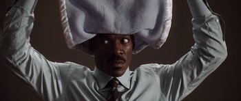 Movie still from “Imagine That” (2009), directed by Karey Kirkpatrick – A man in a dress shirt and tie with a towel on his head; Close Up shot, Low angle