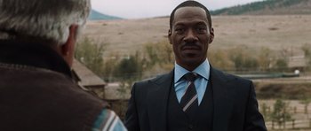 Movie still from “Imagine That” (2009), directed by Karey Kirkpatrick – A man wearing a suit and tie standing in front of a field; Close Up shot, Over the shoulder angle