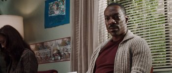 Movie still from “Imagine That” (2009), directed by Karey Kirkpatrick – A man sitting in a chair in a living room; Close Up shot, Over the shoulder angle