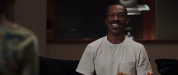 Movie still from “Imagine That” (2009), directed by Karey Kirkpatrick – A man sitting on a couch smiling for the camera; Close Up shot, Over the shoulder angle